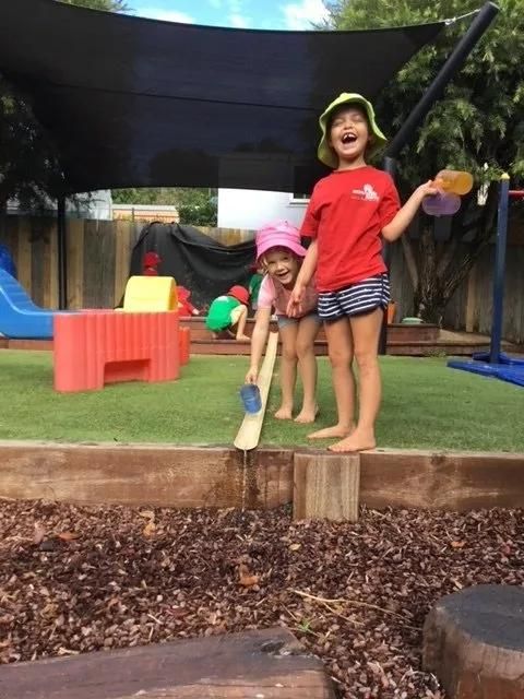 Two Little Girls Are Playing In A Playground And One Is Holding A Watering Can — Moruya Drive Child Care Centre In Port Macquarie, NSW