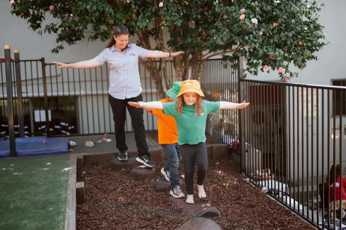 A Woman And Two Children Are Balancing On A Tire In A Playground — Moruya Drive Child Care Centre In Port Macquarie, NSW
