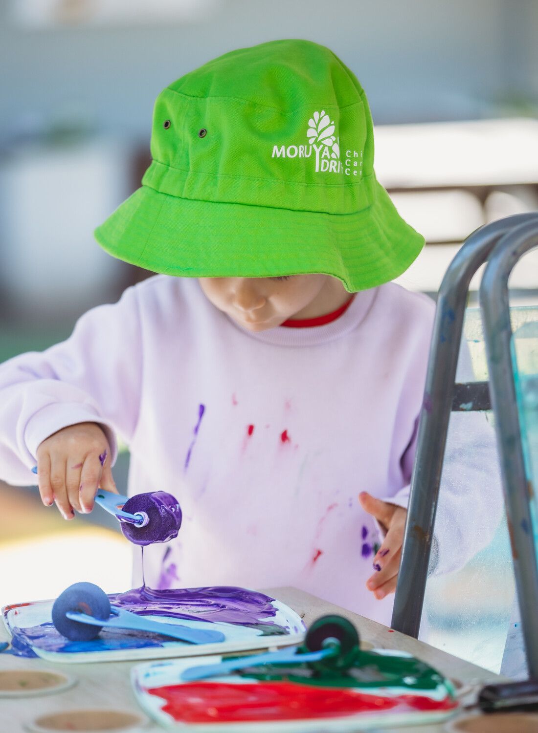 A child wearing a green hat is playing with paint — Moruya Drive Child Care Centre In Port Macquarie, NSW