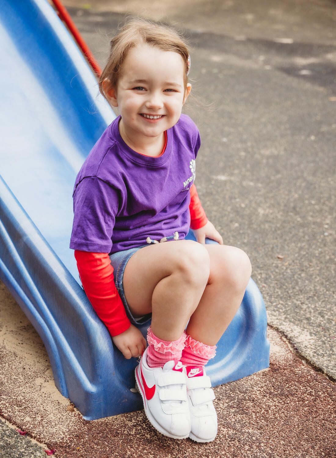 A little girl is sitting on a slide at a playground — Moruya Drive Child Care Centre In Port Macquarie, NSW