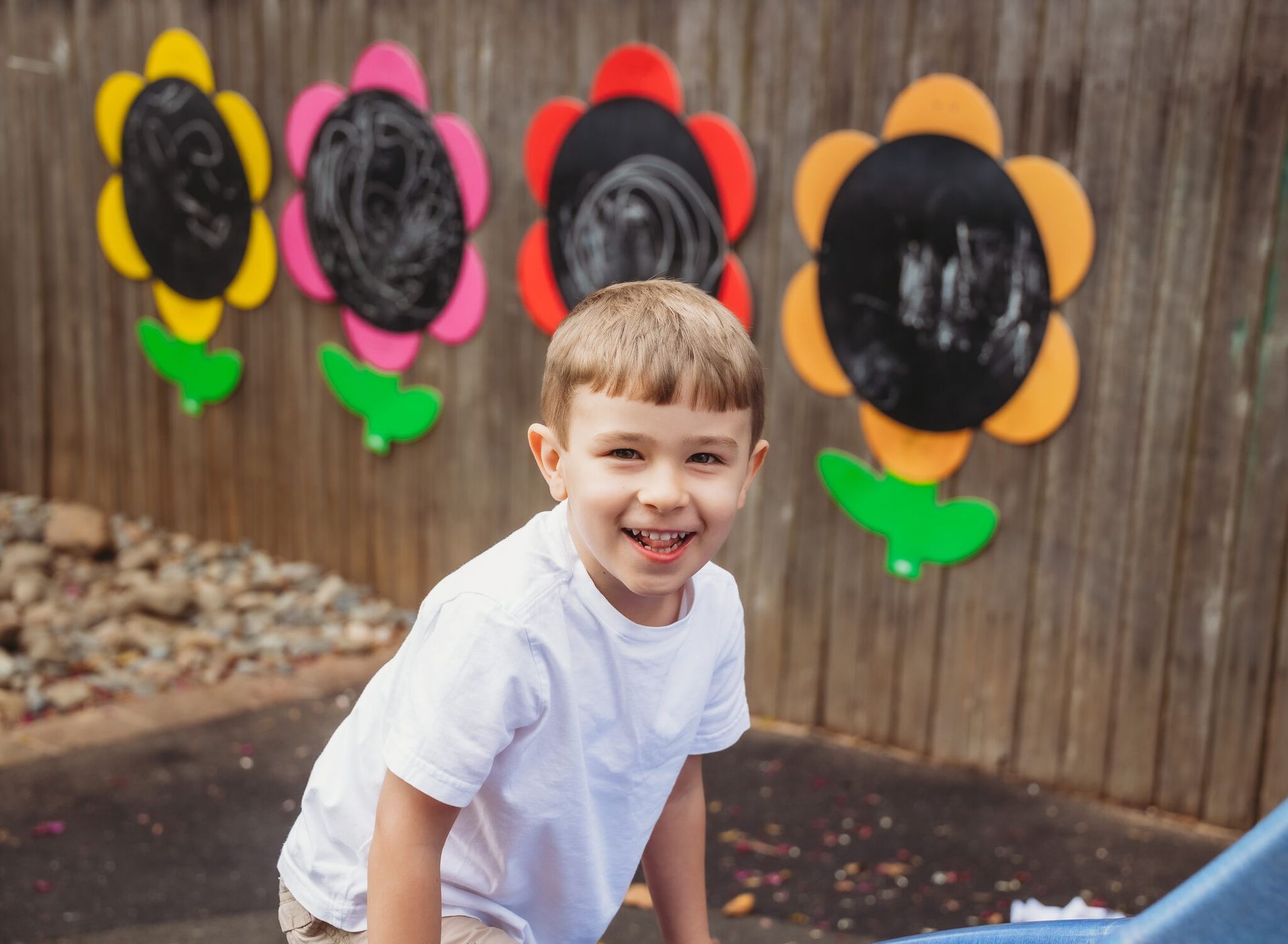 A young boy is standing in front of a fence with flowers painted on it — Moruya Drive Child Care Centre In Port Macquarie, NSW