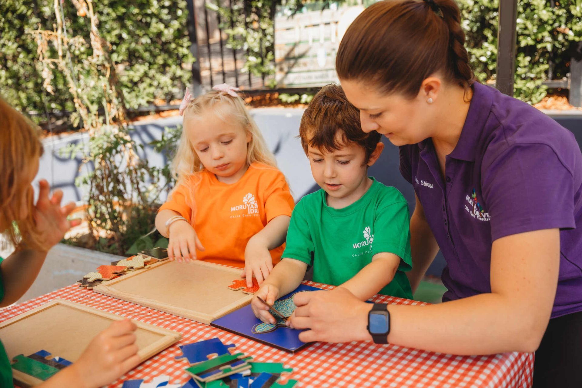 A Group Of Children Are Sitting At A Table Clapping Their Hands — Moruya Drive Child Care Centre In Port Macquarie, NSW