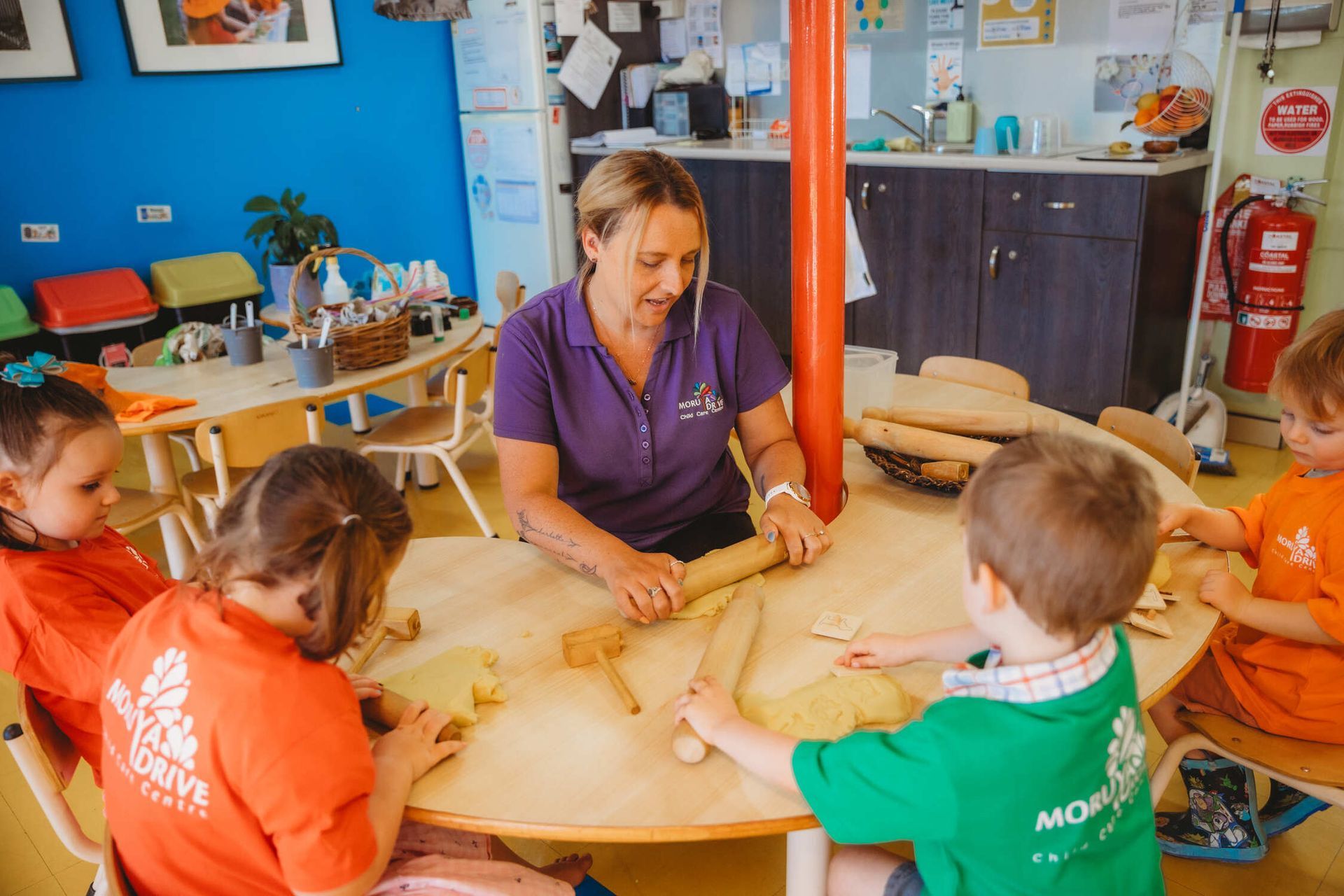 A woman is sitting at a table with a group of children — Moruya Drive Child Care Centre In Port Macquarie, NSW