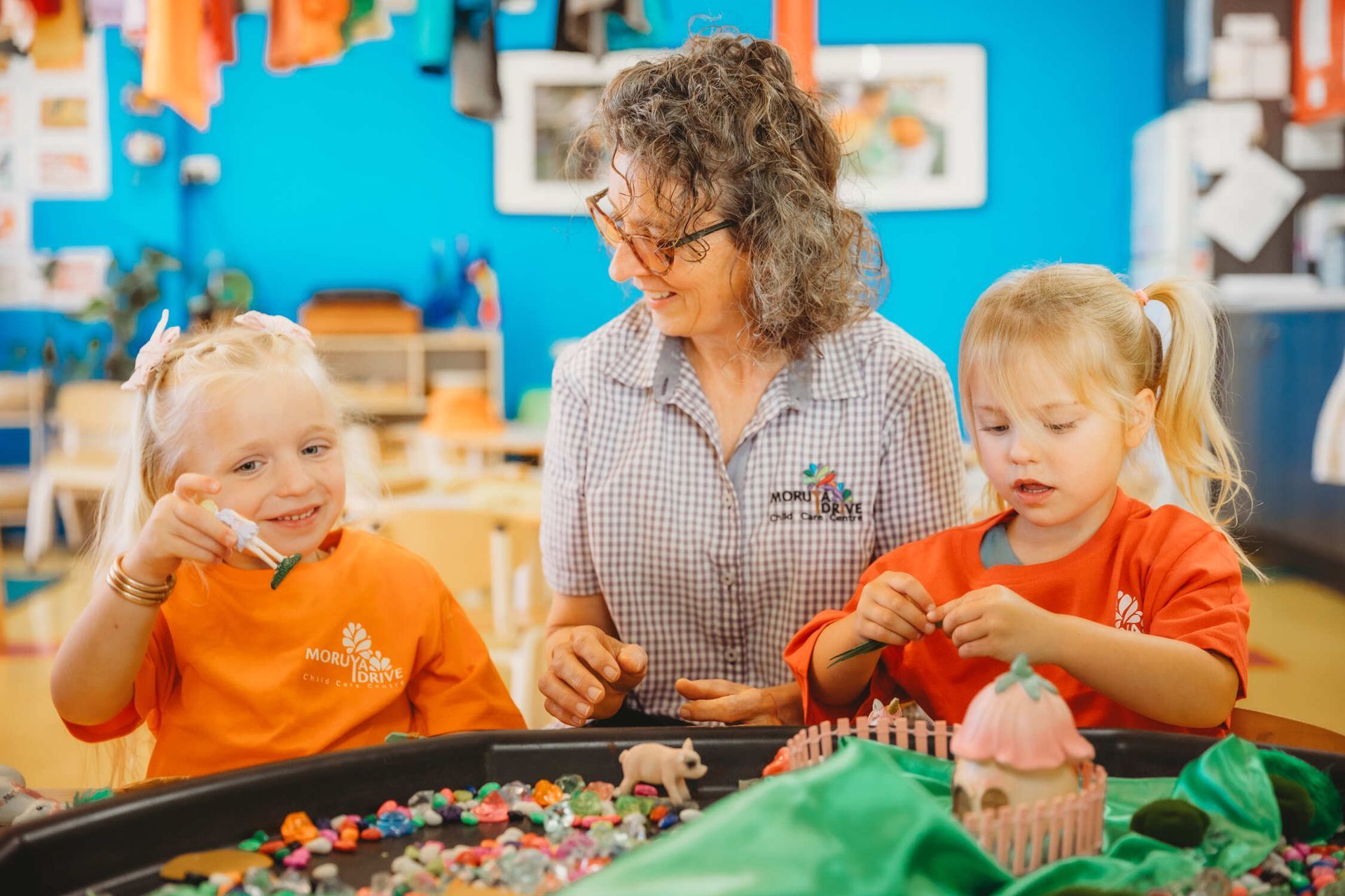 A woman is playing with two young girls in a classroom — Moruya Drive Child Care Centre In Port Macquarie, NSW