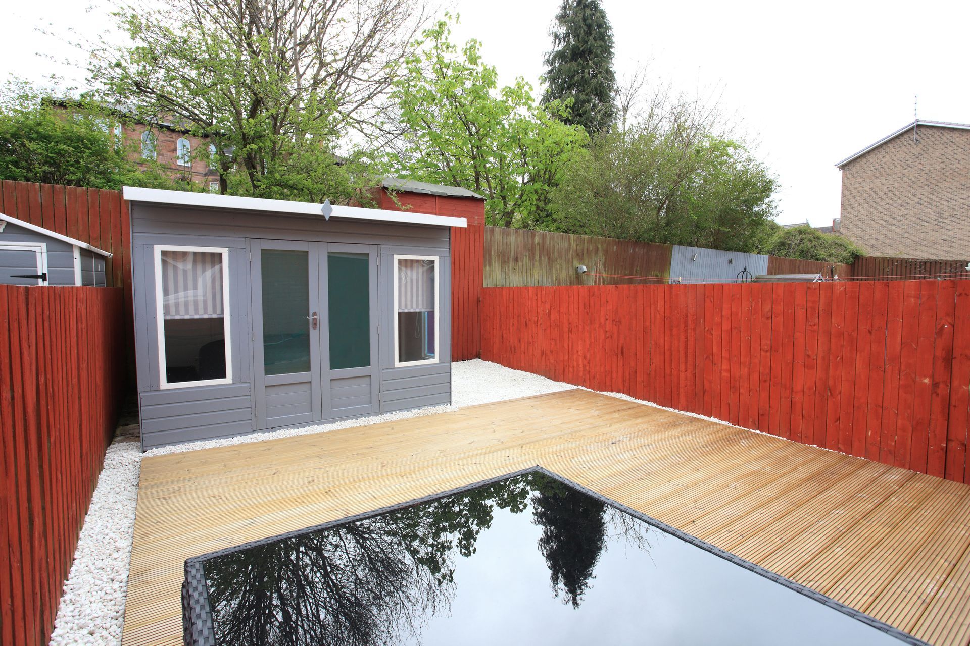 A deck in a backyard with a pool and a red fence