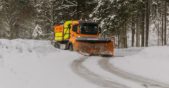 A snow plow is driving down a snow covered road.