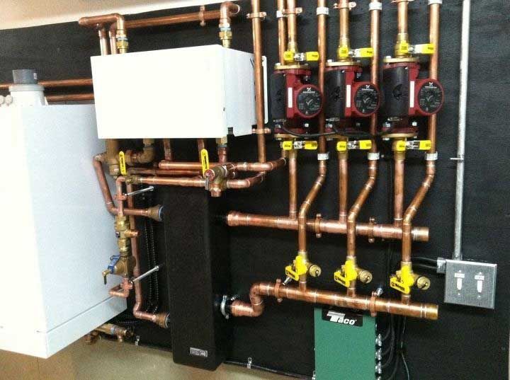 Copper plumbing and pumps on a black wall; part of a heating system.