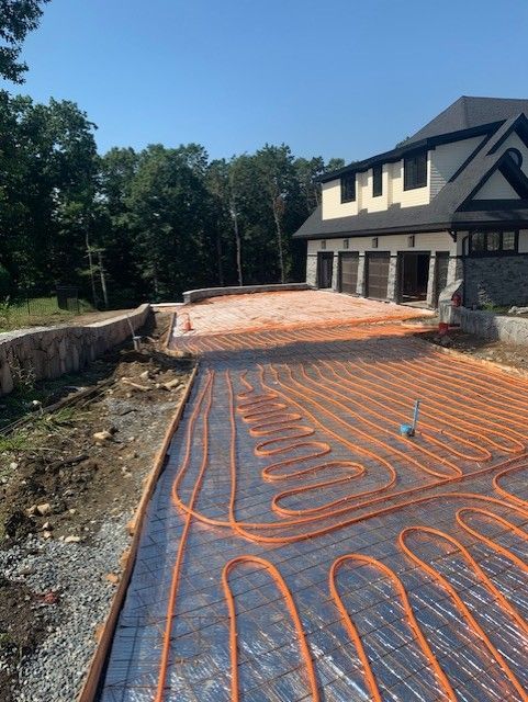 Driveway with orange heating tubes installed, large house in the background.