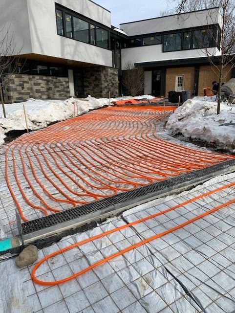 Orange radiant heating tubes laid on wire mesh in front of a modern house with snow.