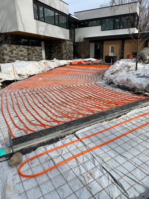 Orange heating tubes laid on mesh in front of a building. Snow on the sides.
