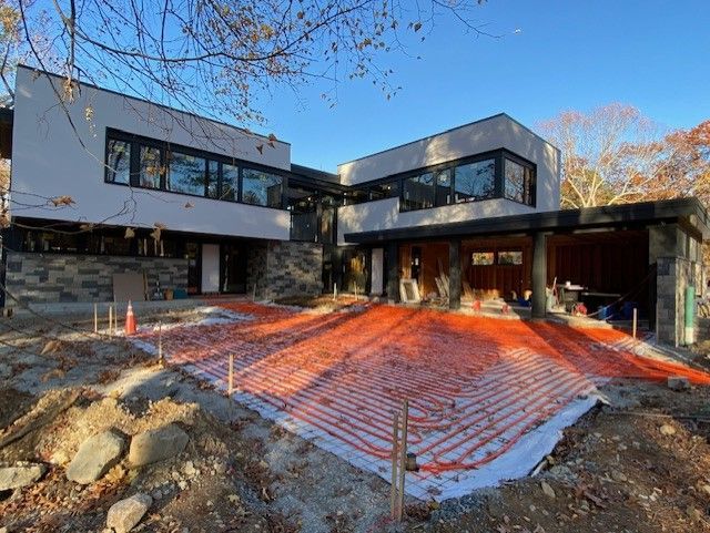 Modern house under construction; orange radiant floor tubing laid out in front. Blue sky.
