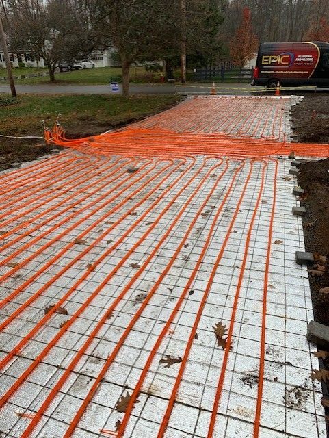 Orange radiant heat tubing laid over wire mesh on a driveway, ready for concrete.