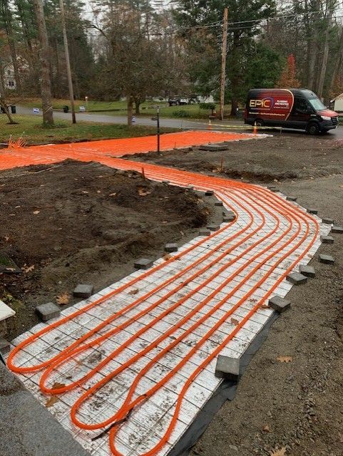 Orange radiant heat tubing laid on a driveway, ready for concrete. A work van is parked nearby.