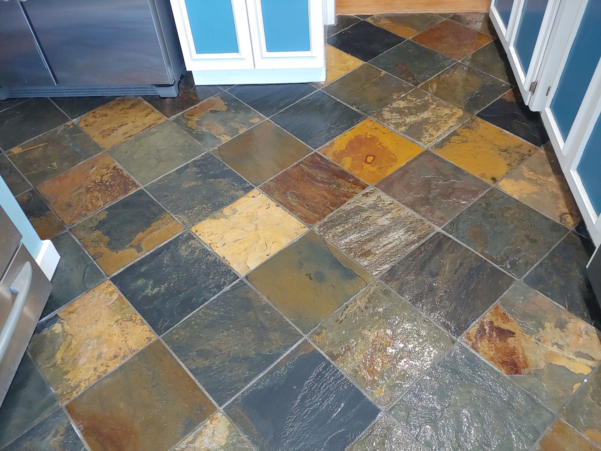 A person wearing bright orange rubber gloves is using a hose to clean the tile floor.