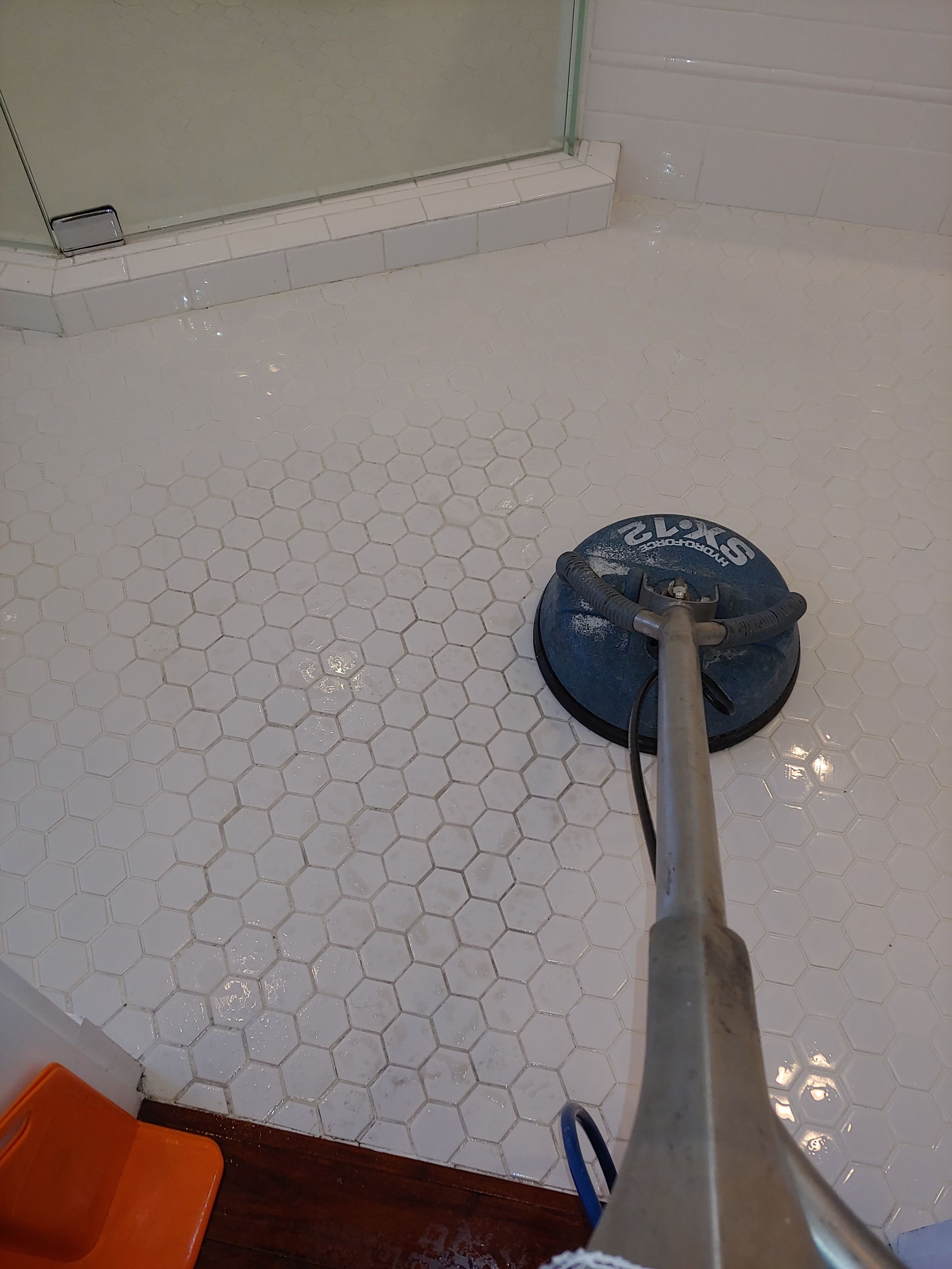 Professional cleaner meticulously scrubbing grout lines with a specialized brush and foamy soap on a sleek gray tiled bathroom floor.