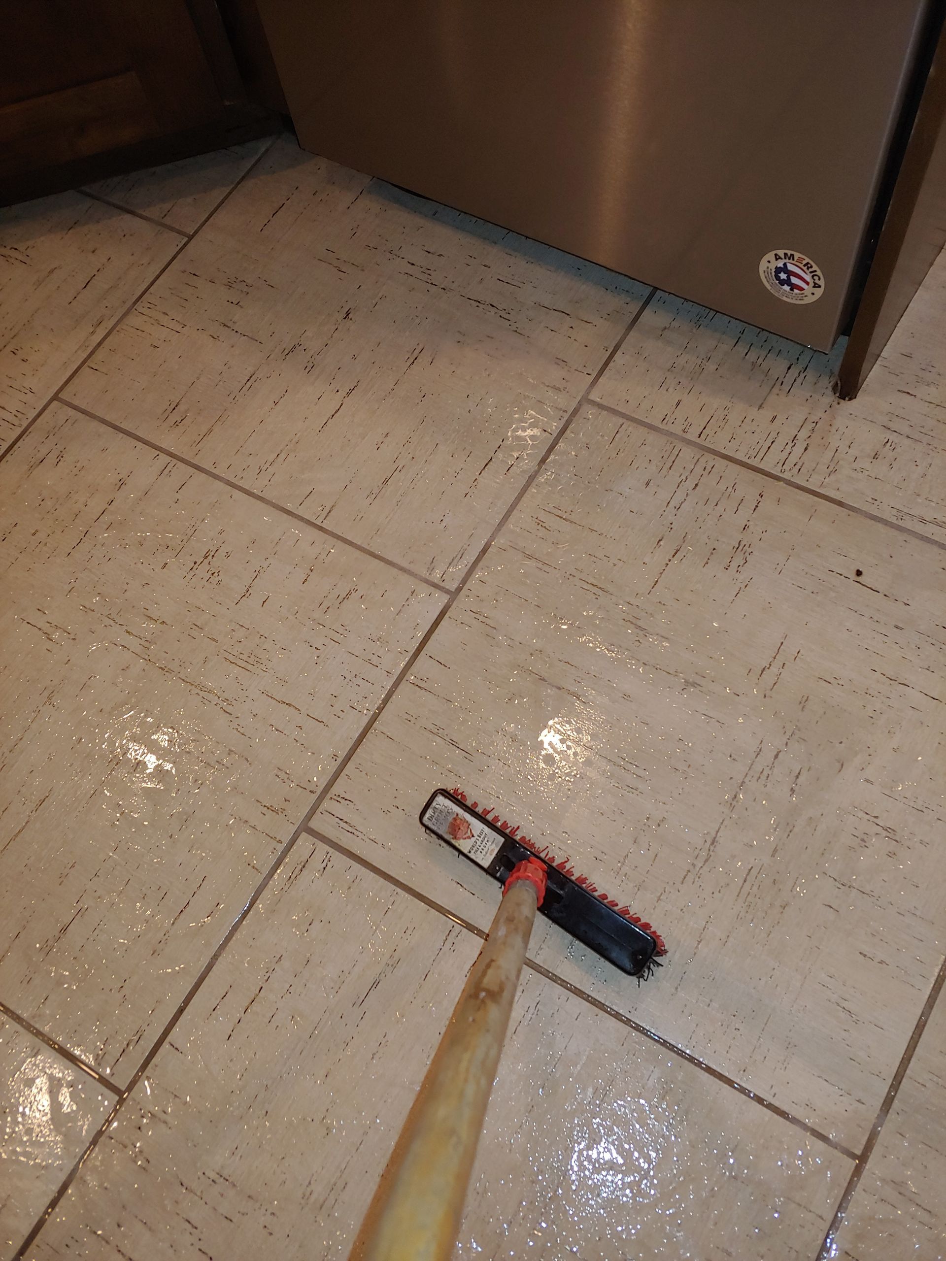 A broom is laying on a tiled floor next to a refrigerator.