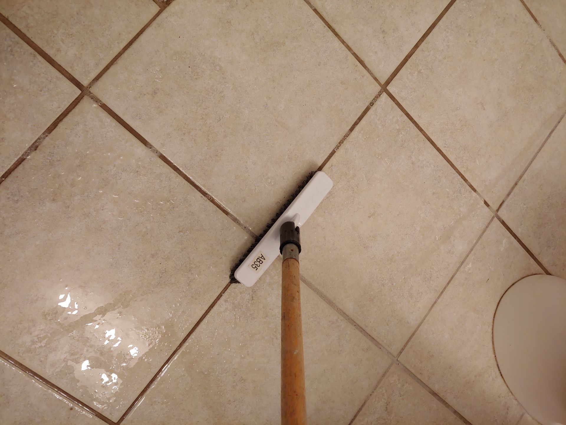 A person wearing bright orange rubber gloves is using a hose to clean the tile floor.