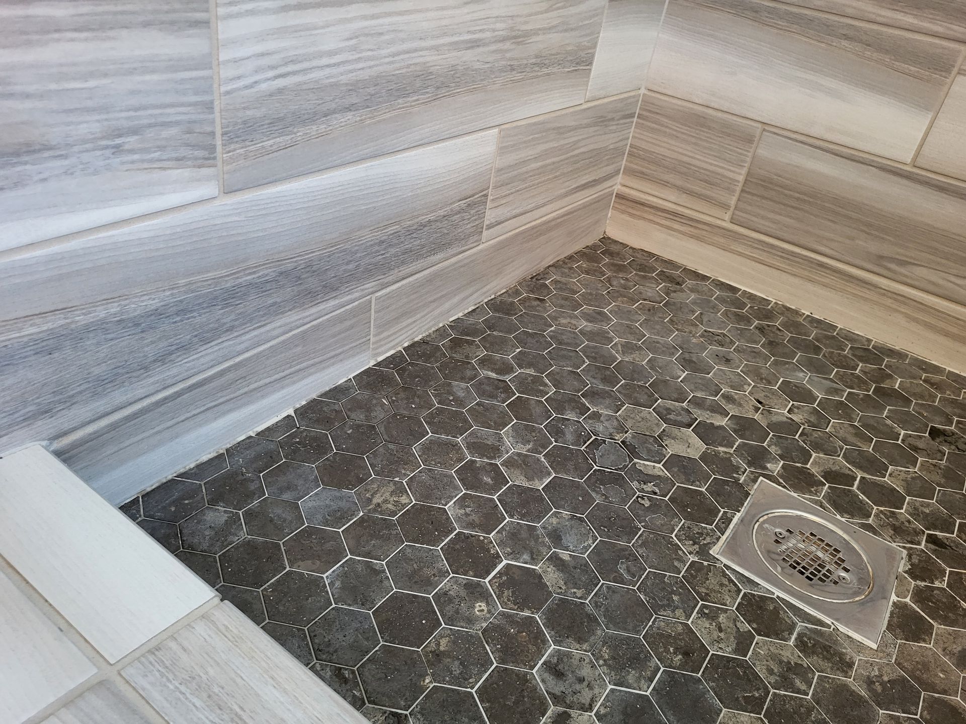 Professional cleaner meticulously scrubbing grout lines with a specialized brush and foamy soap on a sleek gray tiled bathroom floor.