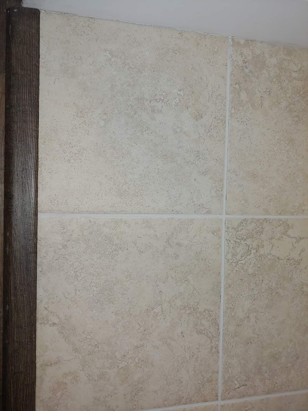 A close up of a tiled wall with a wooden trim.