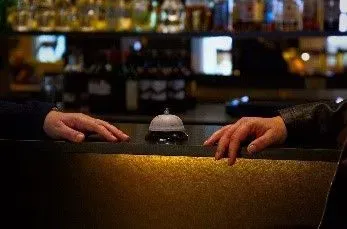 Front desk with a bell in between 2 hands of conceirge attendants ready for service