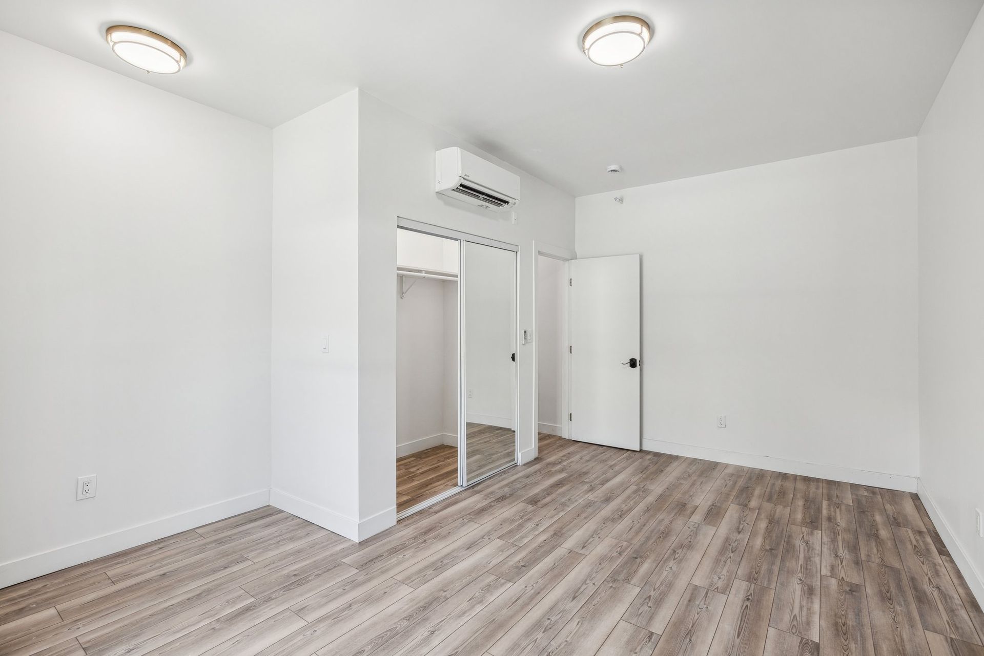 Bright room with wood-style flooring, mirrored closet, and clean design. At The Ansley, managed by SKY Properties, Inc.