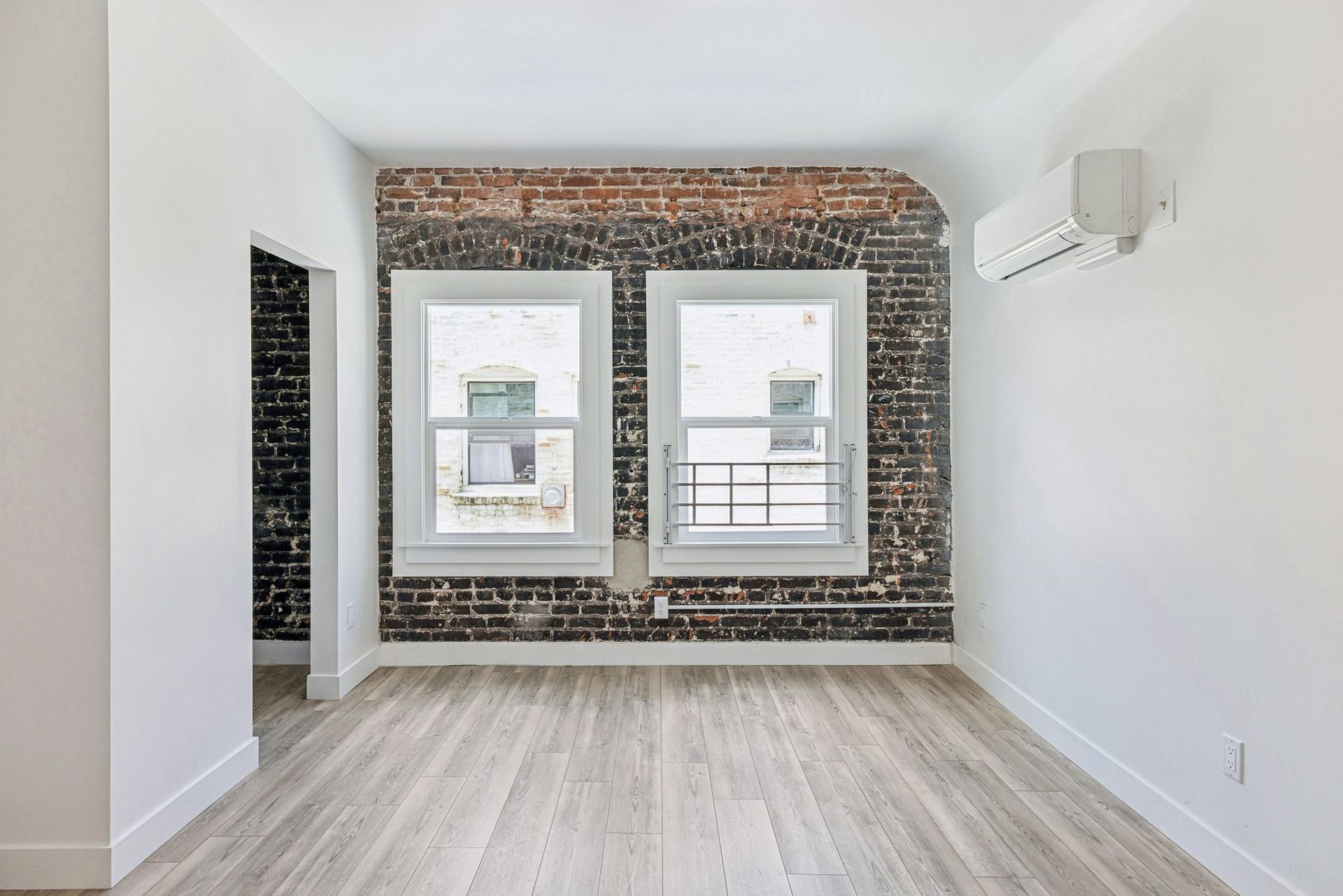 Room with exposed brick accent wall, windows, and wood-style flooring. At The Ansley, managed by SKY Properties, Inc.