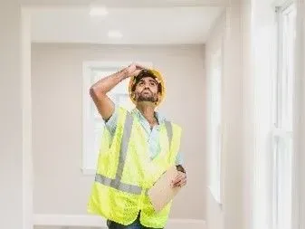 A maintenance worker in reflectorized yellow vest and hard hat inspeting apartment space 