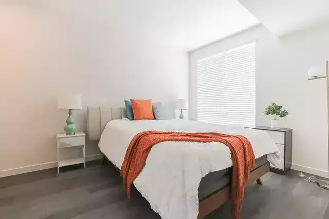 photo of The Centennial's cozy and bright bedroom with a bed, side table and windows with opened blinds