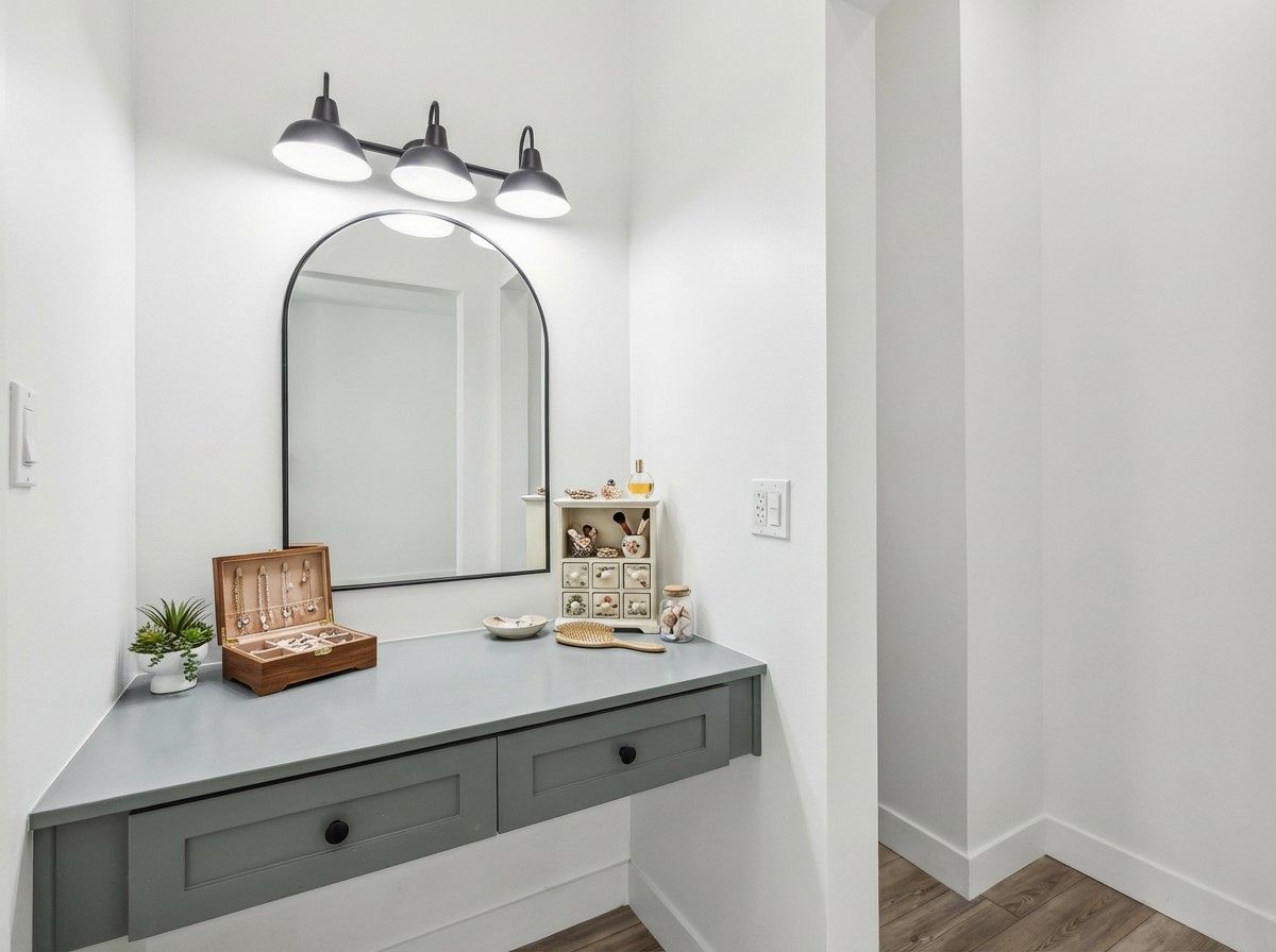 A modern vanity nook with a gray floating desk, arched mirror, black light fixtures, and minimalist decor.