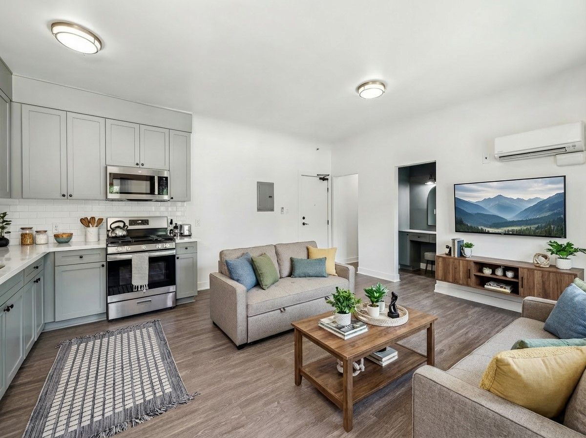 A modern gray vanity area with an arched mirror, built-in drawers, soft lighting, and a pink velvet stool for seating.