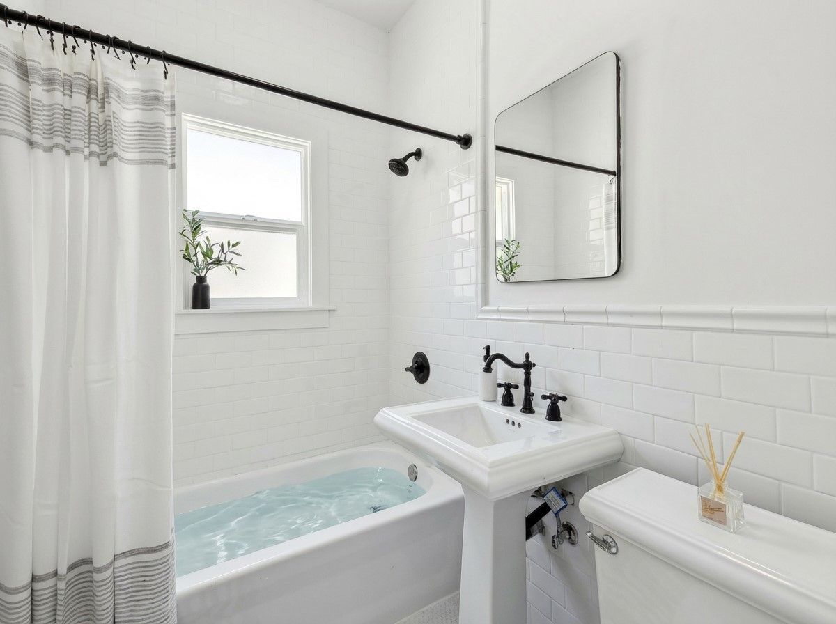 A modern white bathroom with subway tiles, a pedestal sink, black fixtures, and a shower curtain with black trim details.