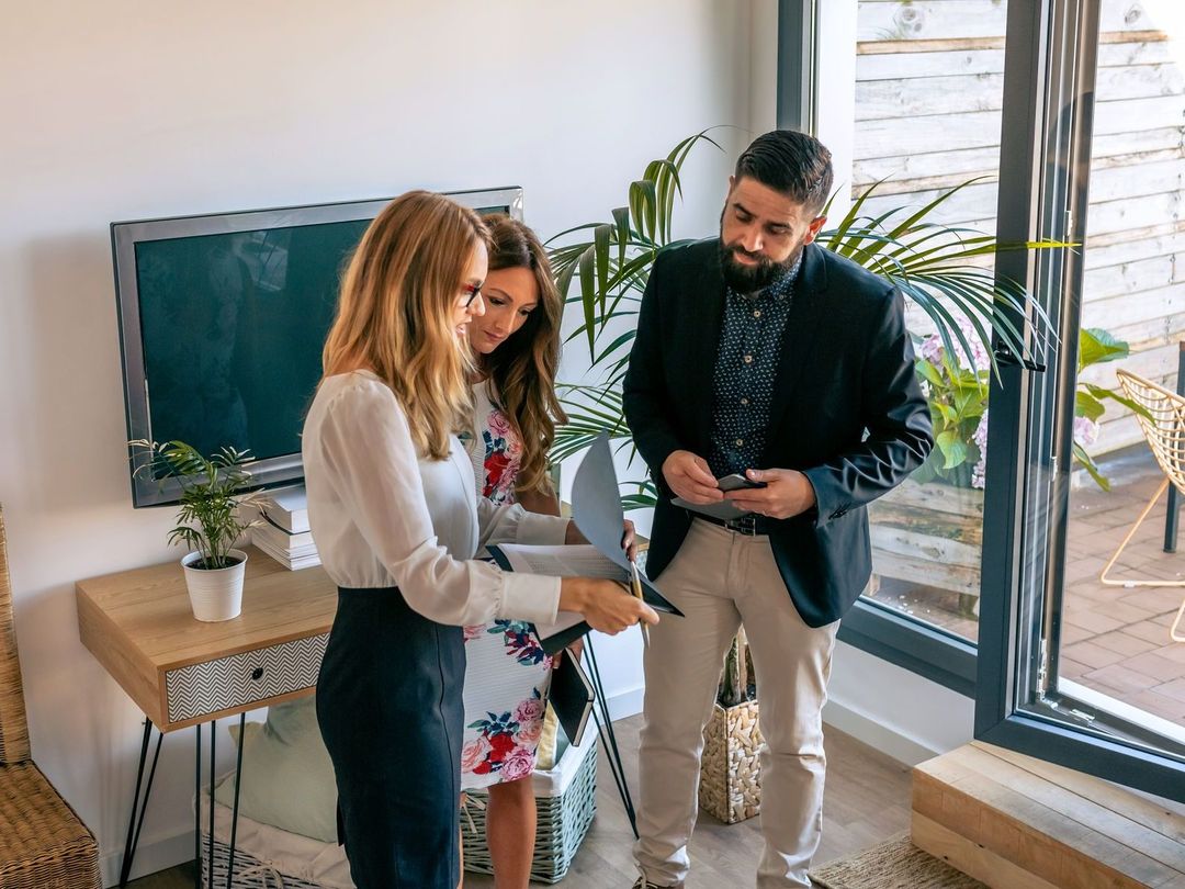 A group of people are standing in a living room looking at a tablet.