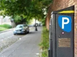 A pay parking sign and booth at the apartment grounds at a street with approching car