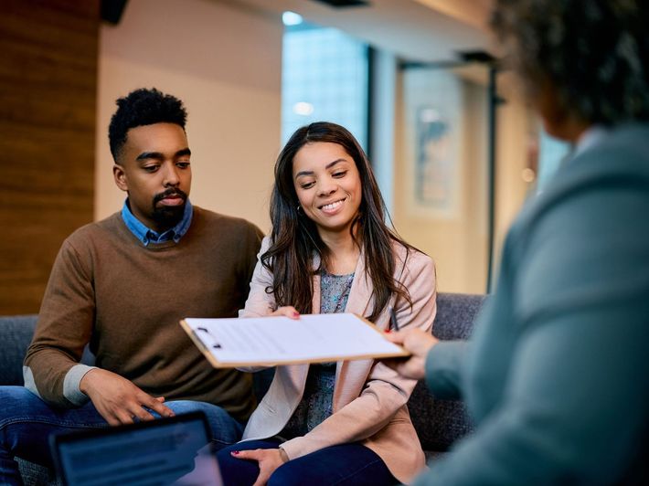A man and a woman are sitting on a couch looking at a clipboard.