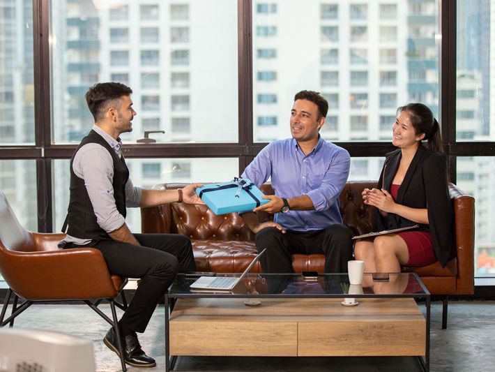 A man giving a gift to a couple while seated on a couch