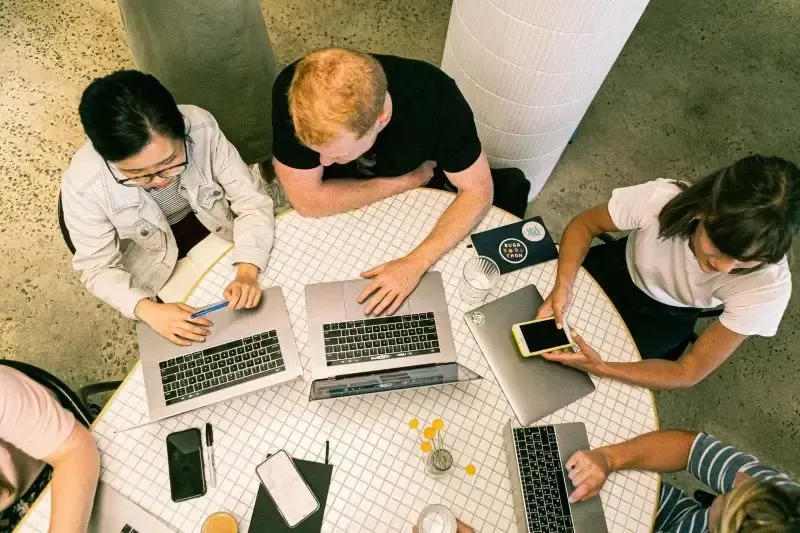 a bird's eye view photo of a small group of property management experts huddled  and, working  on their laptops 