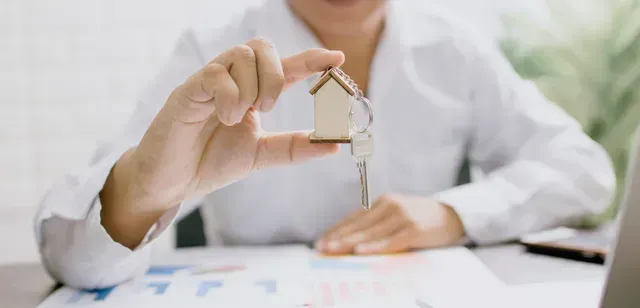 Hands up close holding a key with tiny house keychain implying rent control in Los Angeles