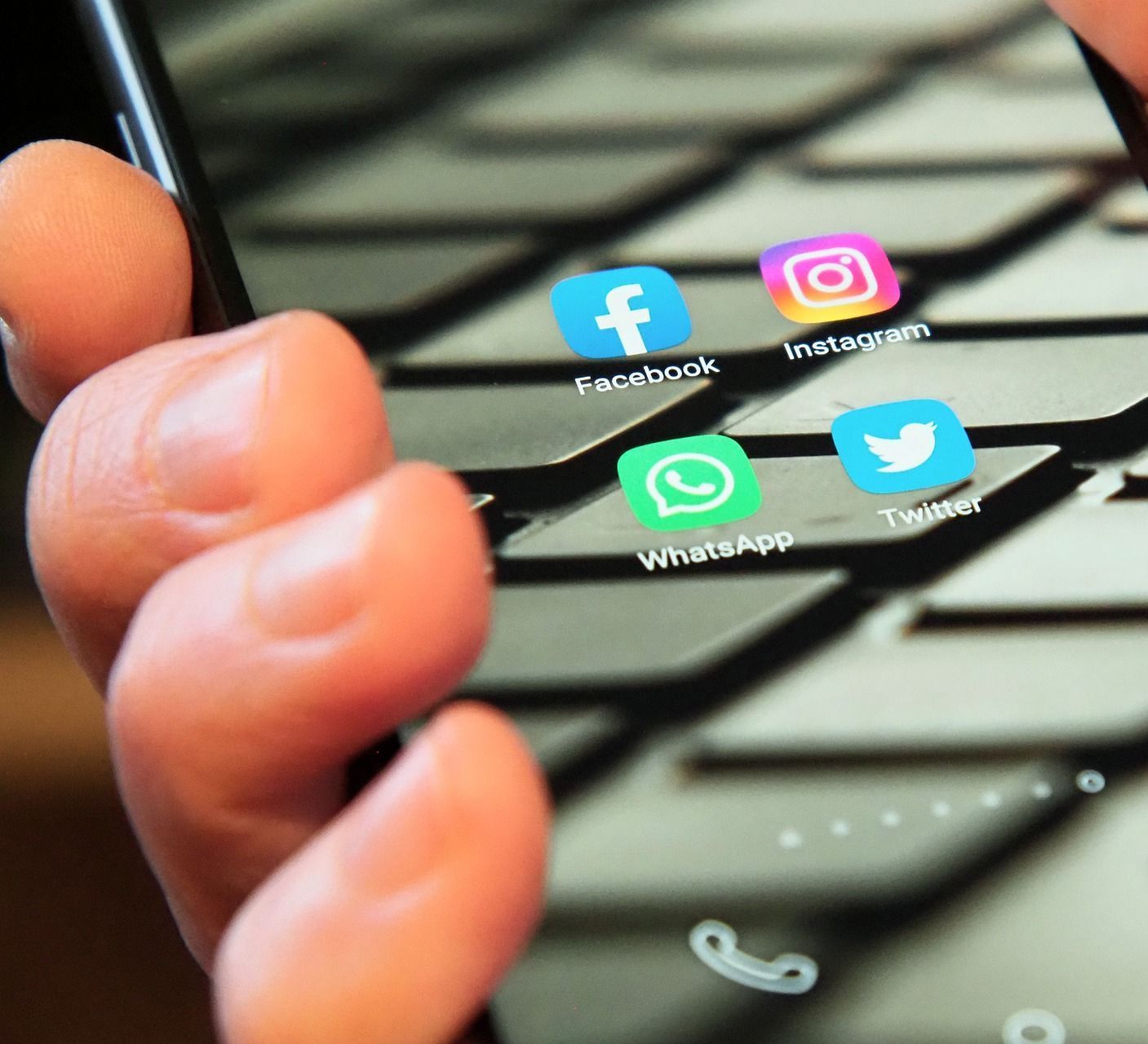 close up image a hand holding a mobile phone with the screen showing four social media icons