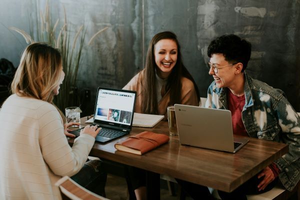 photo of three people smiling and happily chatting while working on their laptops