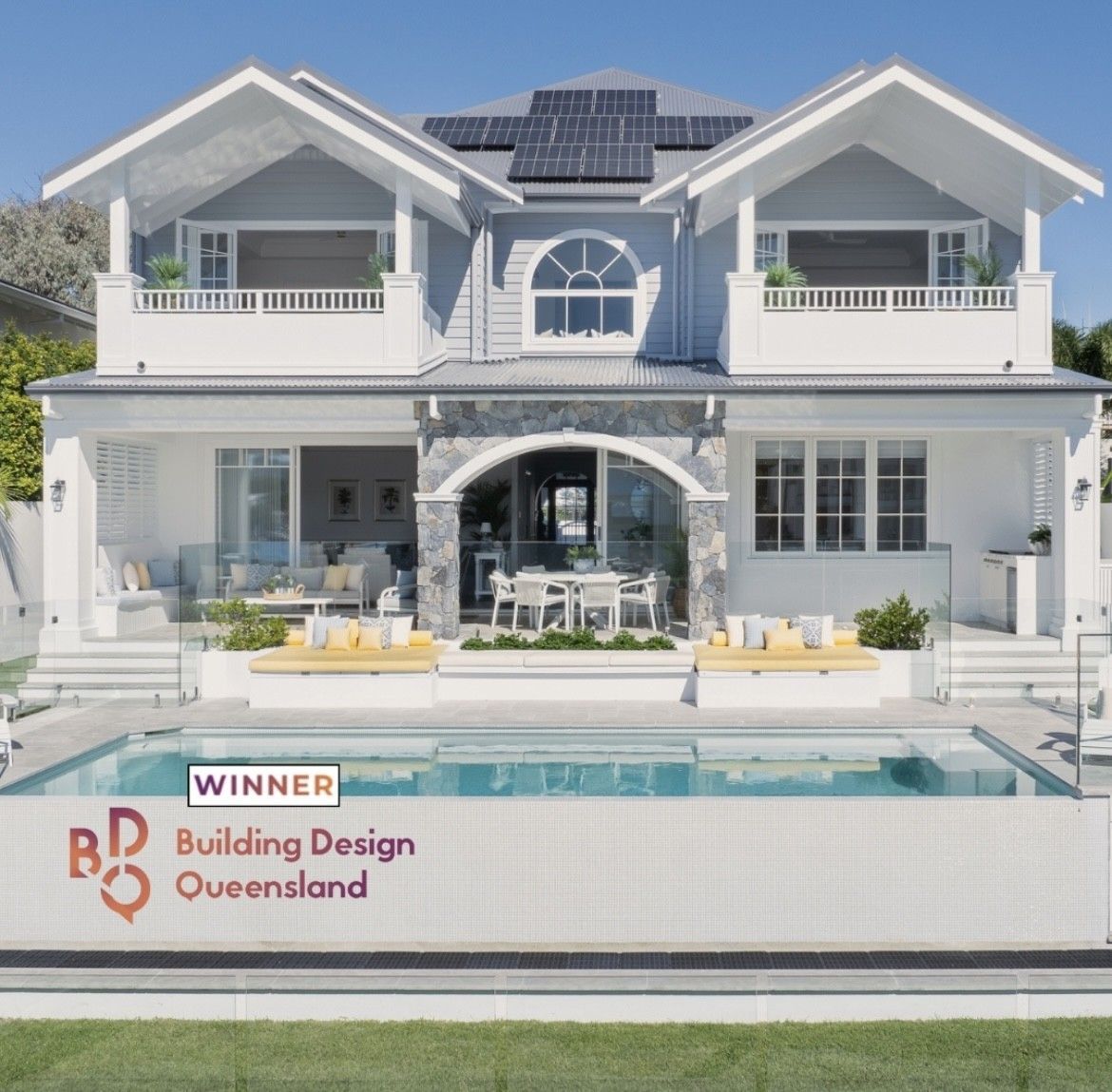 Two-story white house with a pool, sunbeds, and Building Design Queensland award text.