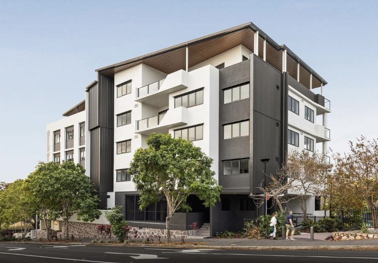 Modern, multi-story apartment building with white and dark gray facades, balconies, and mature trees along the street.