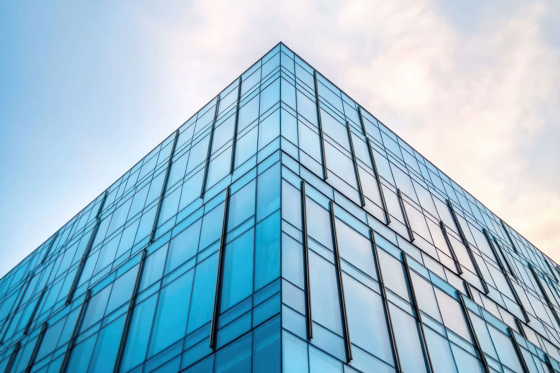 Modern glass-walled building corner against a light blue and white sky. Modern glass-walled building corner against a light blue and white sky.