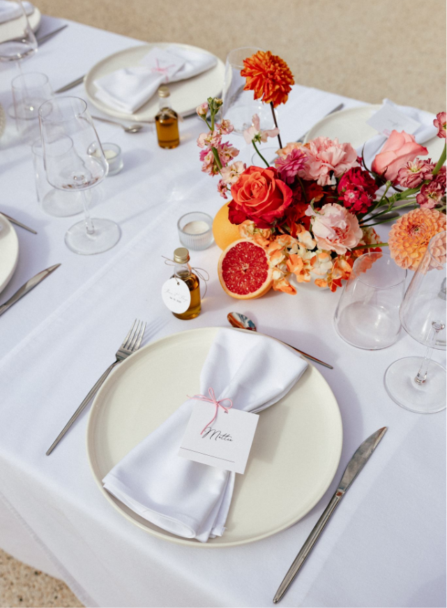 Une longue table avec une nappe blanche est posée devant une grande fenêtre.