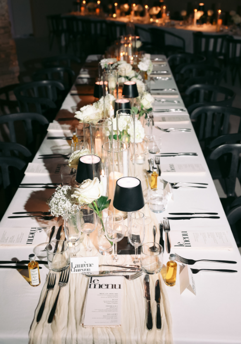 Une longue table avec des assiettes, des verres, des serviettes et des fleurs dessus.