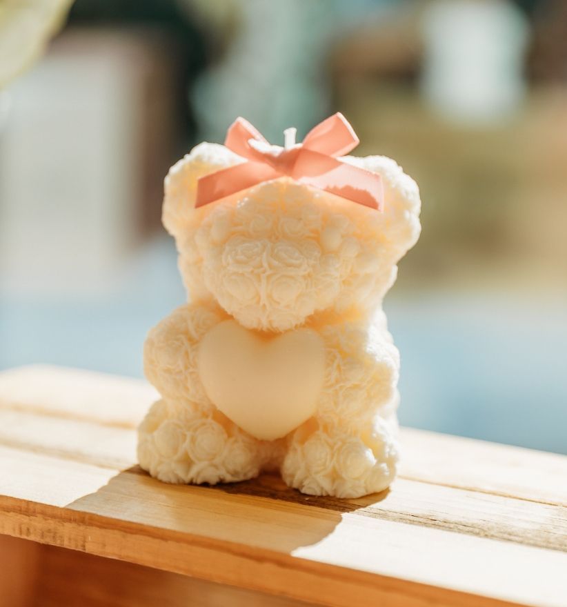 Une bougie en forme d'ours en peluche blanc avec un nœud rose sur la tête