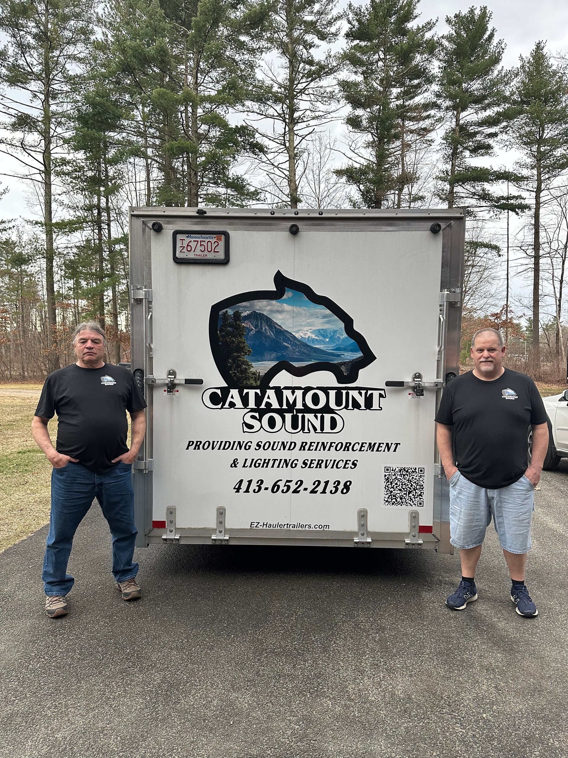 Two men are standing in front of a trailer.