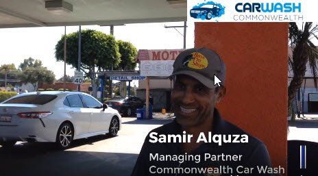 A man is standing in front of a car wash with a car in the background.