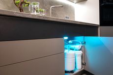 Under-sink water filtration system with blue LED lighting inside a modern kitchen cabinet.