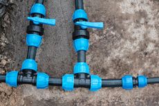 Black polyethylene irrigation pipes connected by blue plastic fittings and two blue-handled ball valves on sandy ground.