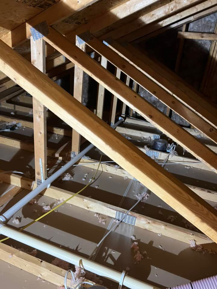 The ceiling of an attic with wooden beams and pipes.